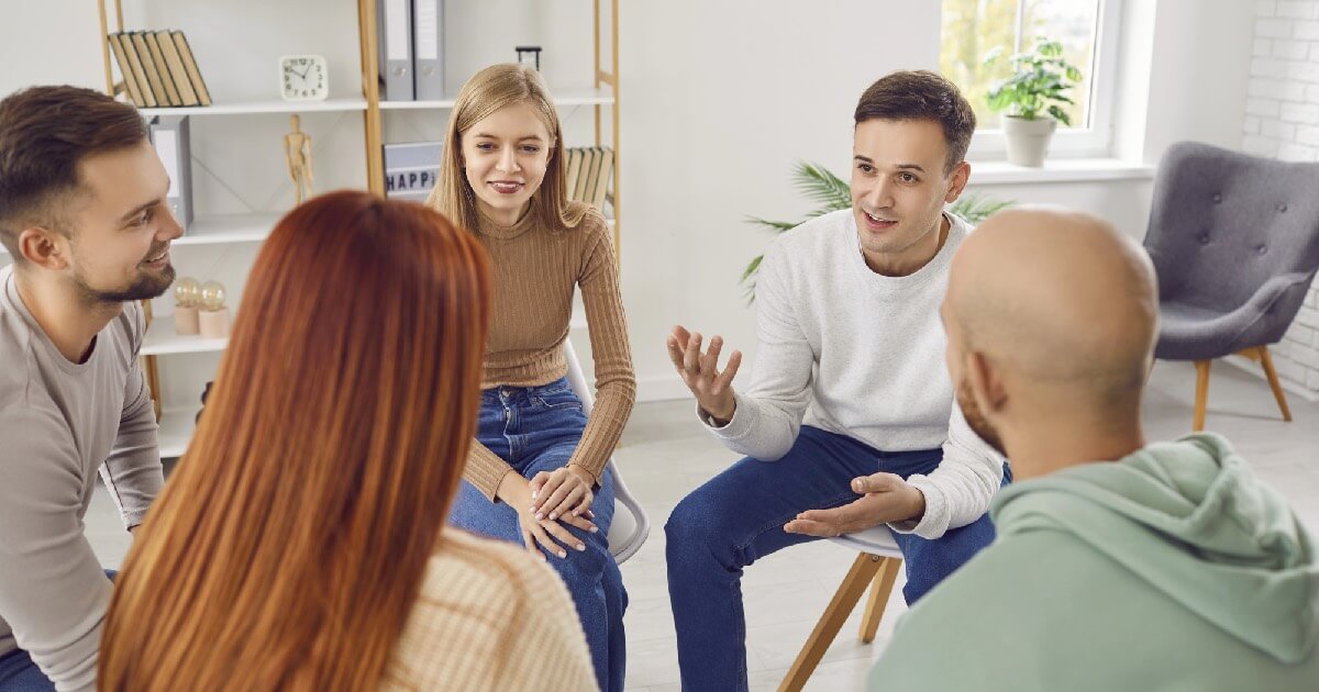 A man speaks while seated in a small group therapy session, engaging with others in a supportive environment.
